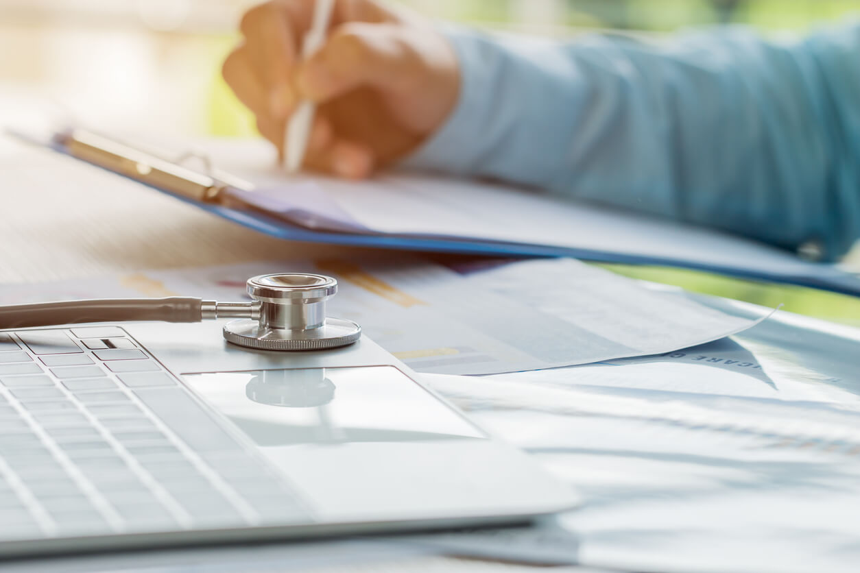 Provider doing paperwork with laptop and stethoscope